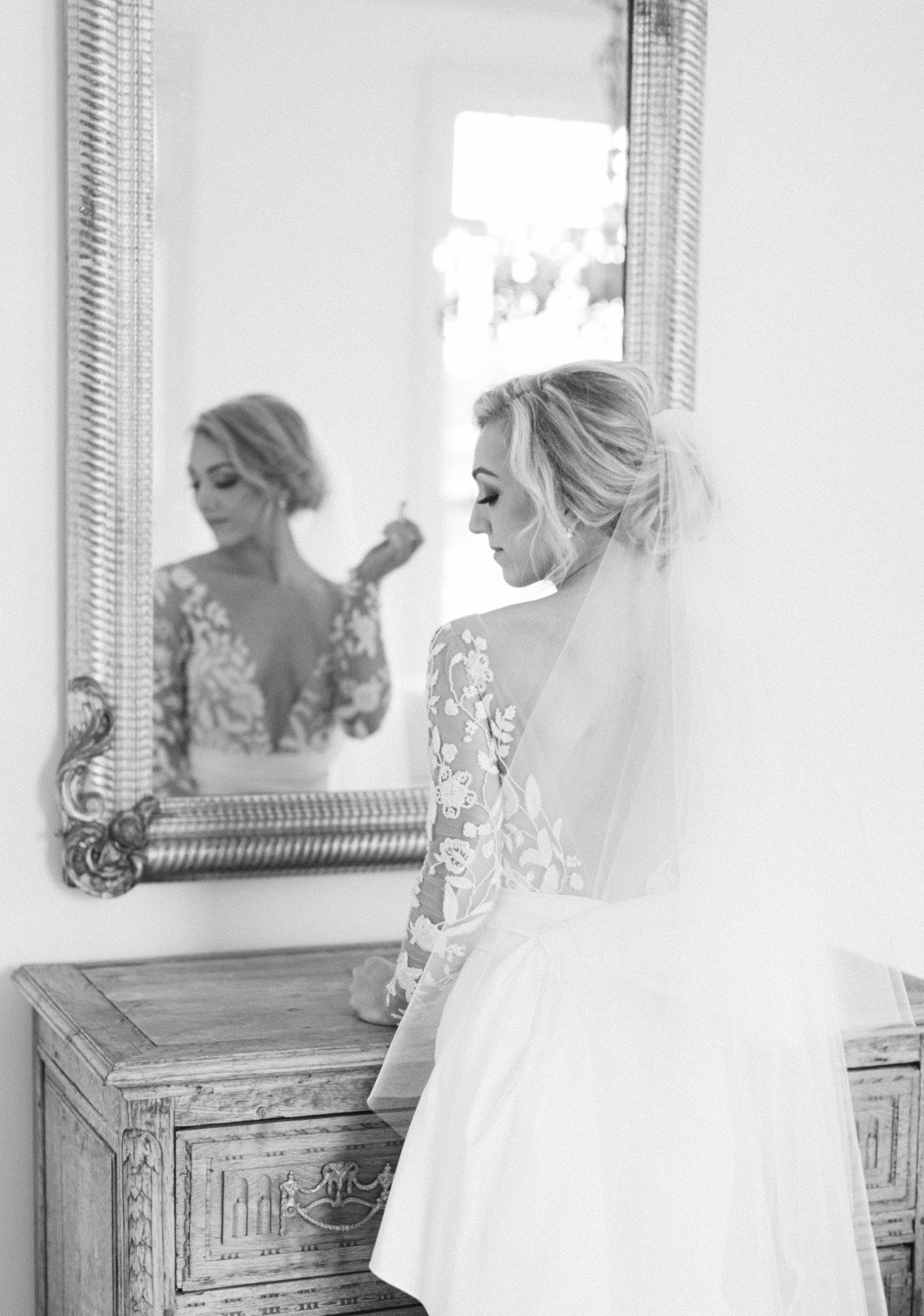 Reflection of bride putting on lipstick in mirror. 
