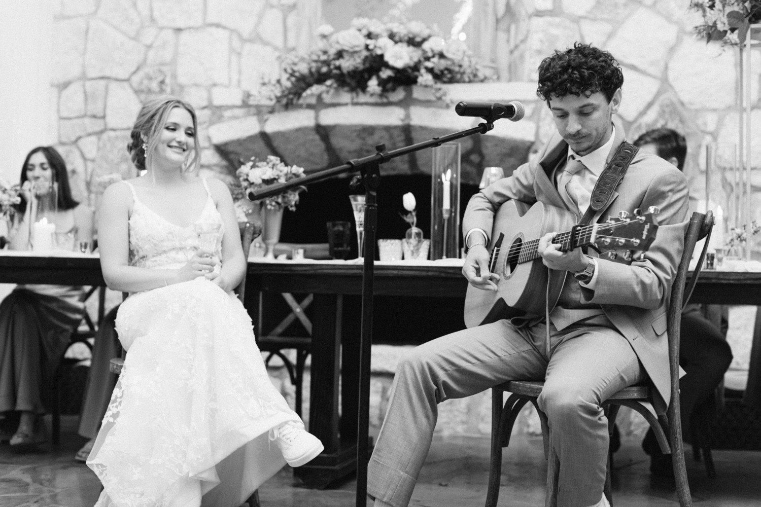 Groom playing song on guitar for bride during wedding reception.