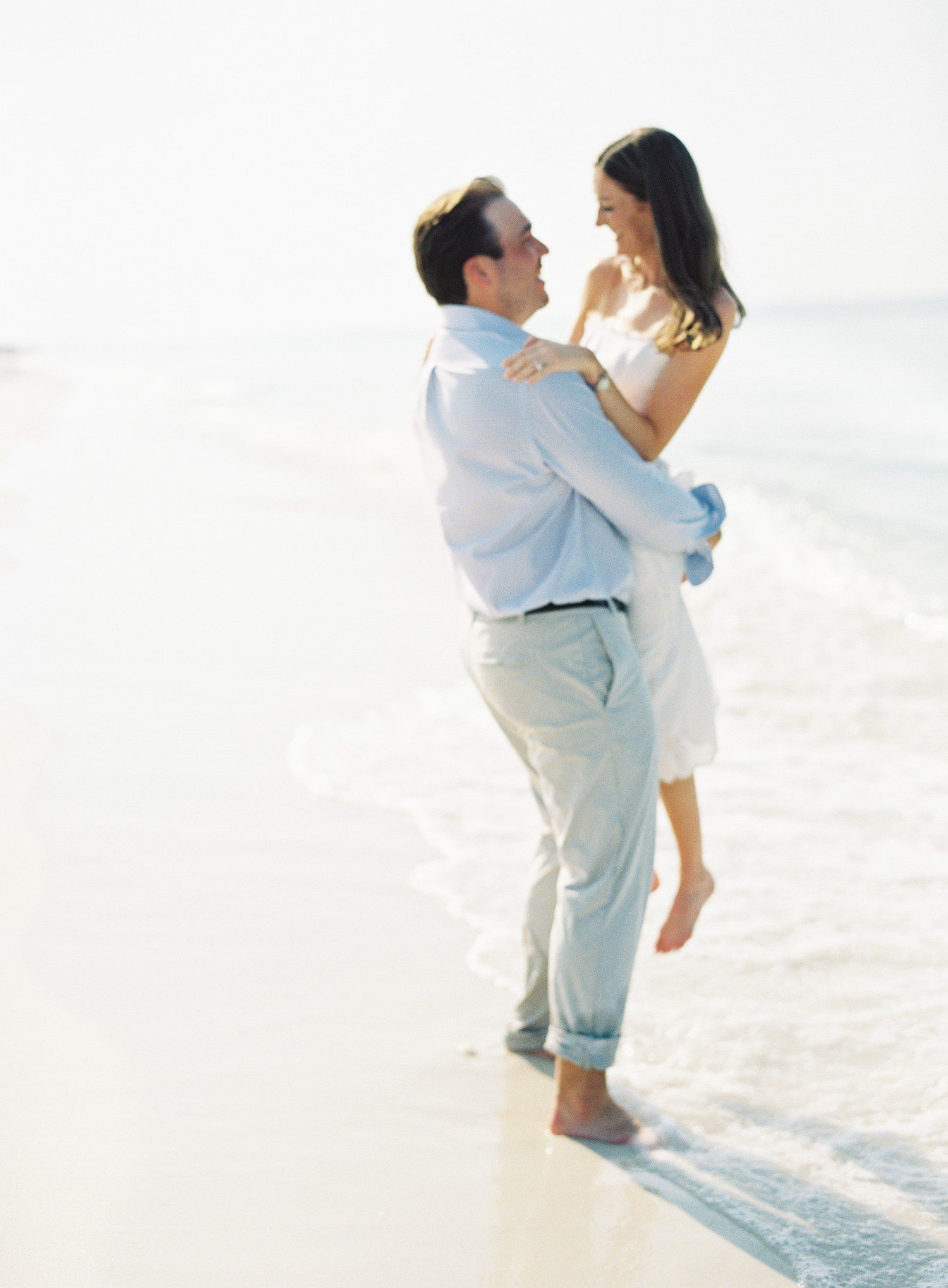 Guy picking up girl during engagement photos on the beach. 