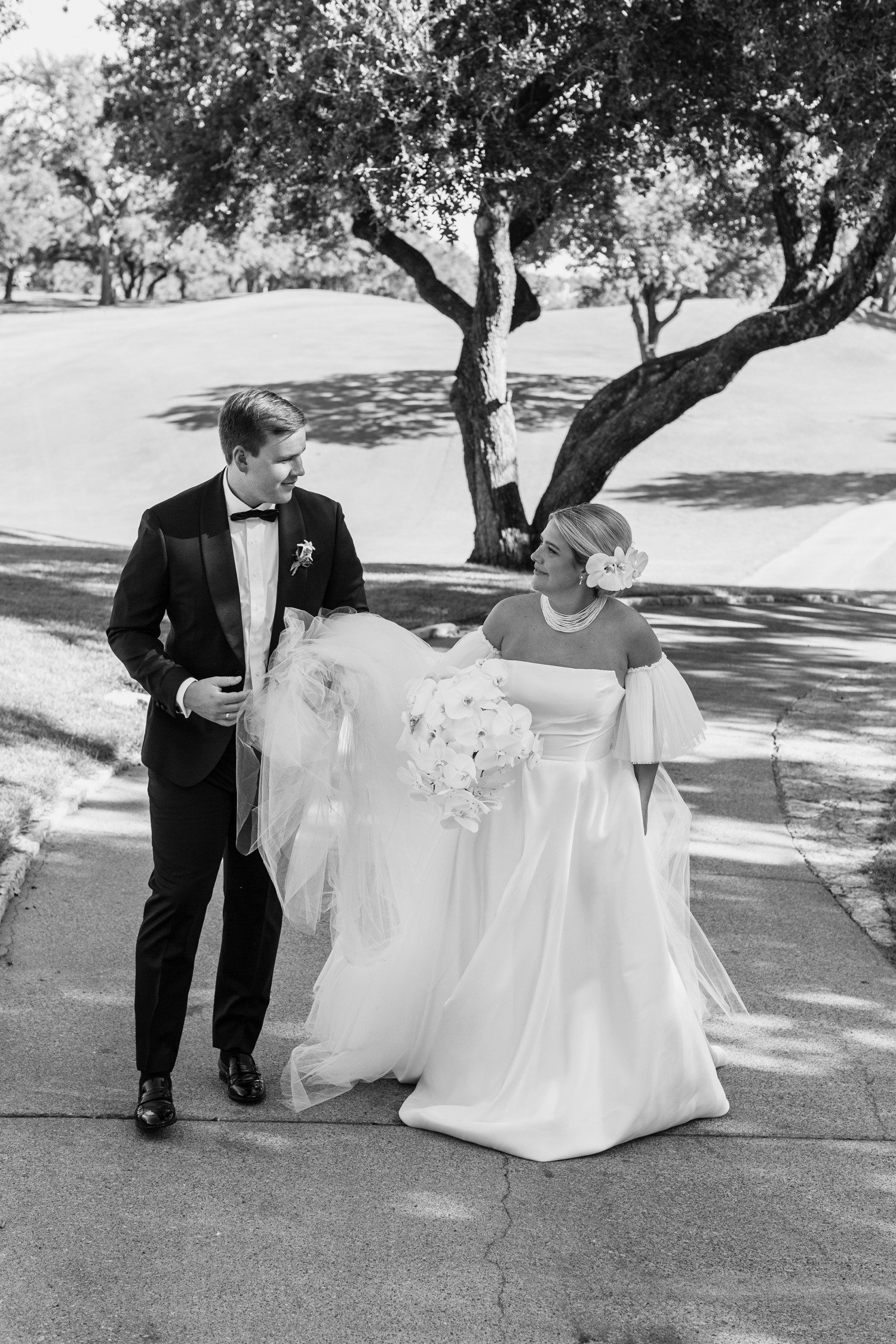 Groom holding bride's dress as they walk together at Austin Country Club.