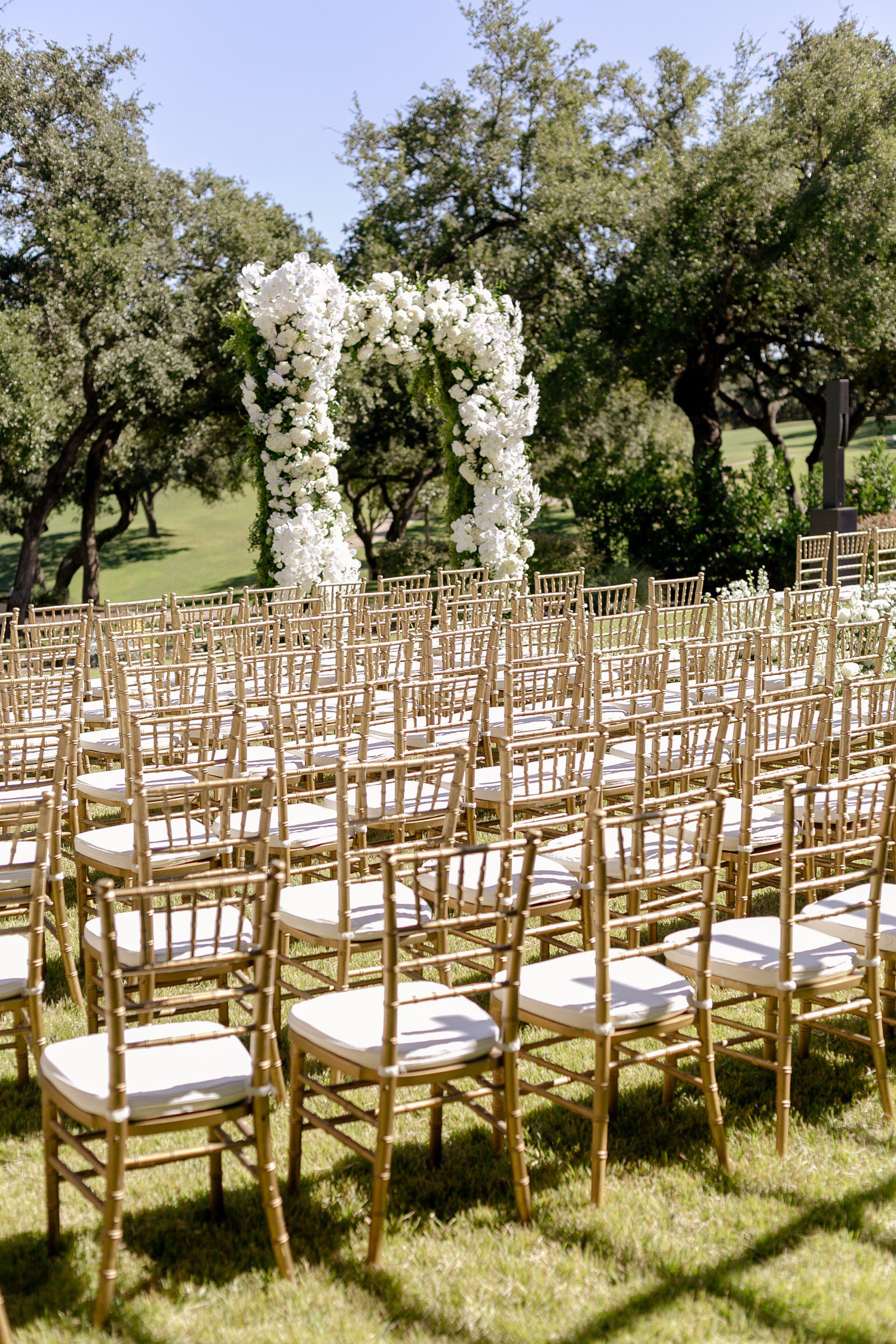 Outdoor wedding ceremony at Austin Country Club with arch of white flowers.