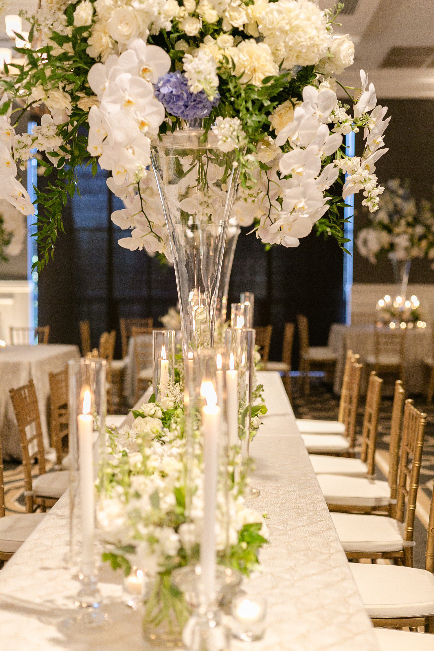Wedding reception table with white candles and tall floral centerpieces.