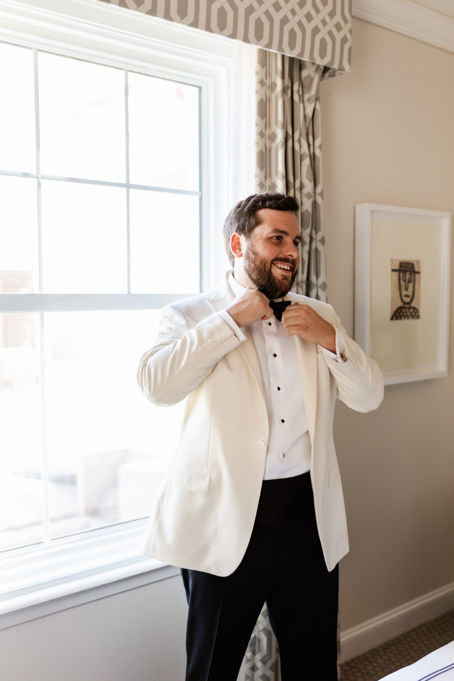 Groom getting ready in white suit jacket.