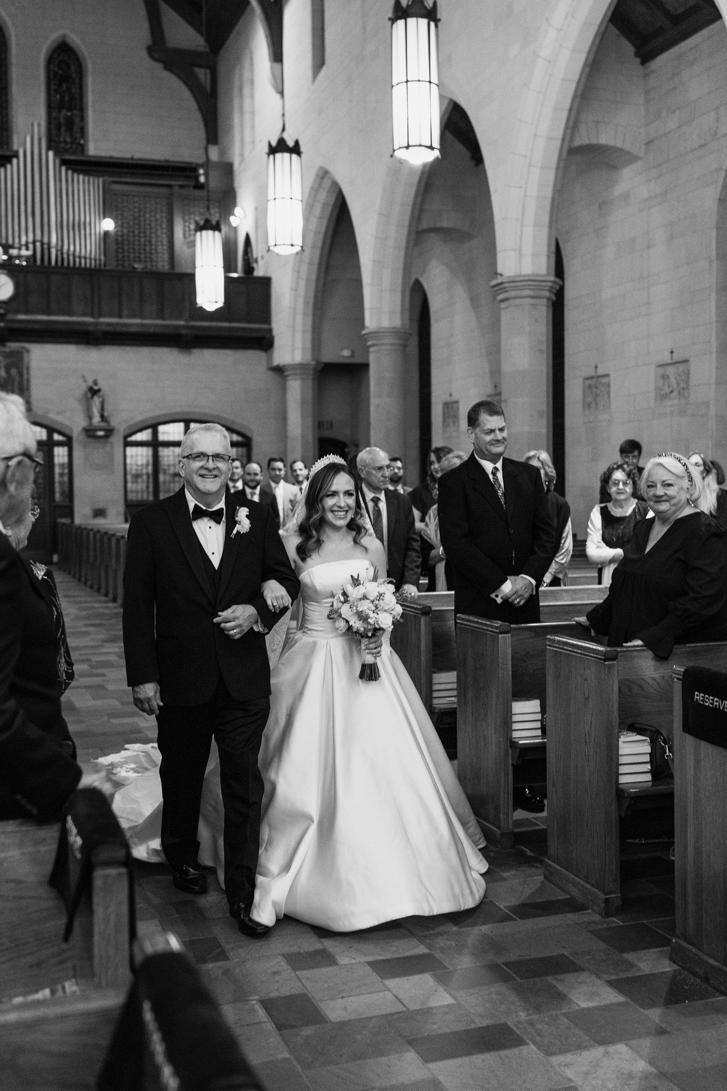 Bride and father walking down the aisle smiling at Holy Rosary Church.
