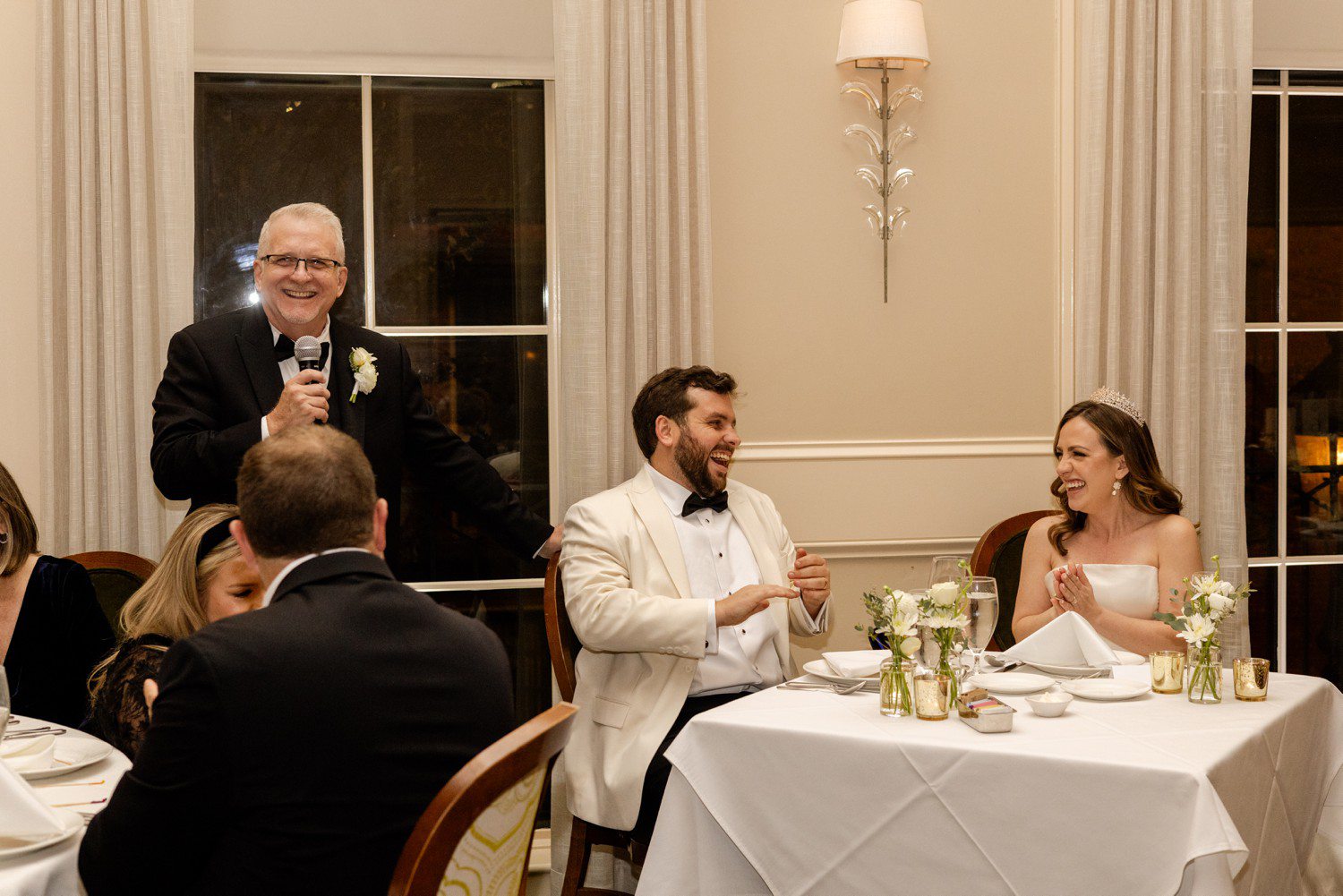 Bride and groom laughing during toast at wedding.