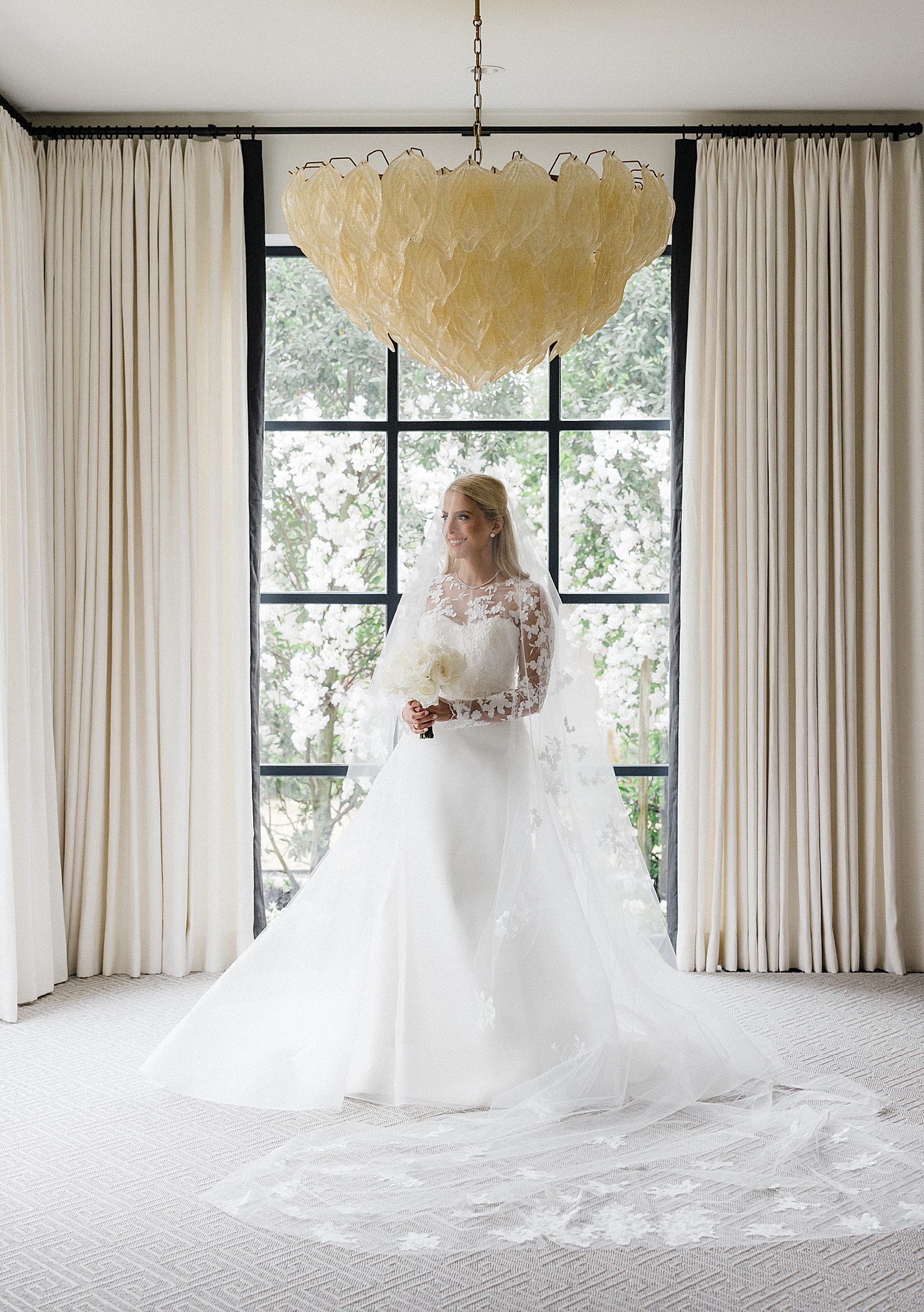 Bride holding bouquet under large chandelier, with veil and train spread out around her