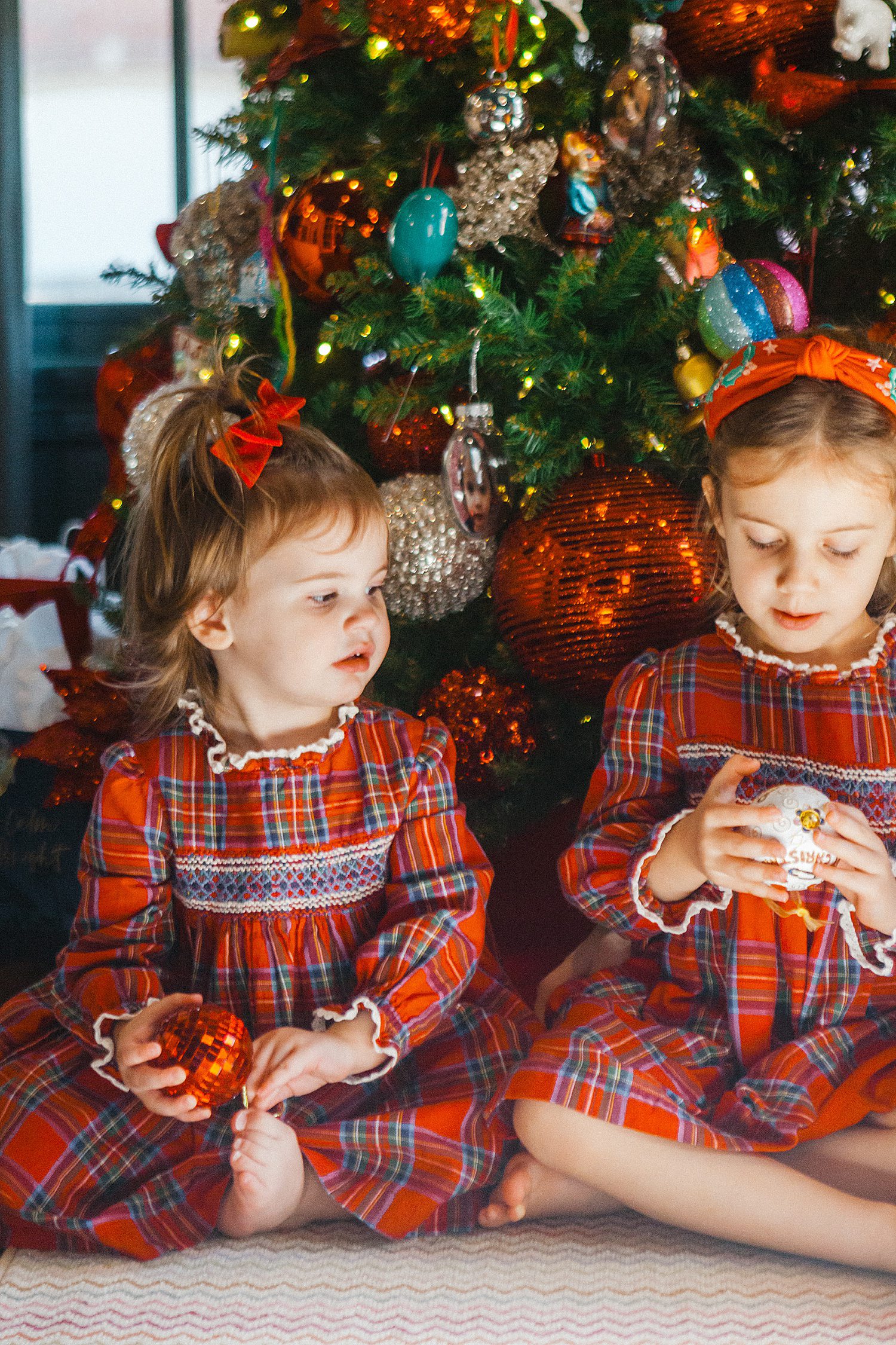 Photo of sisters in plaid dresses in front of a christmas tree