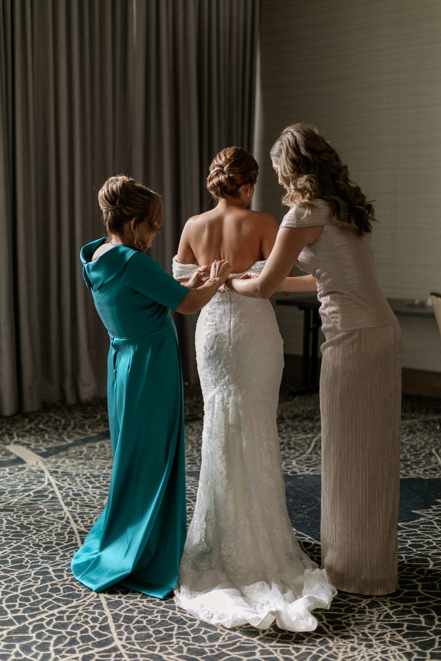 Mother and sister of bride helping her put gown on