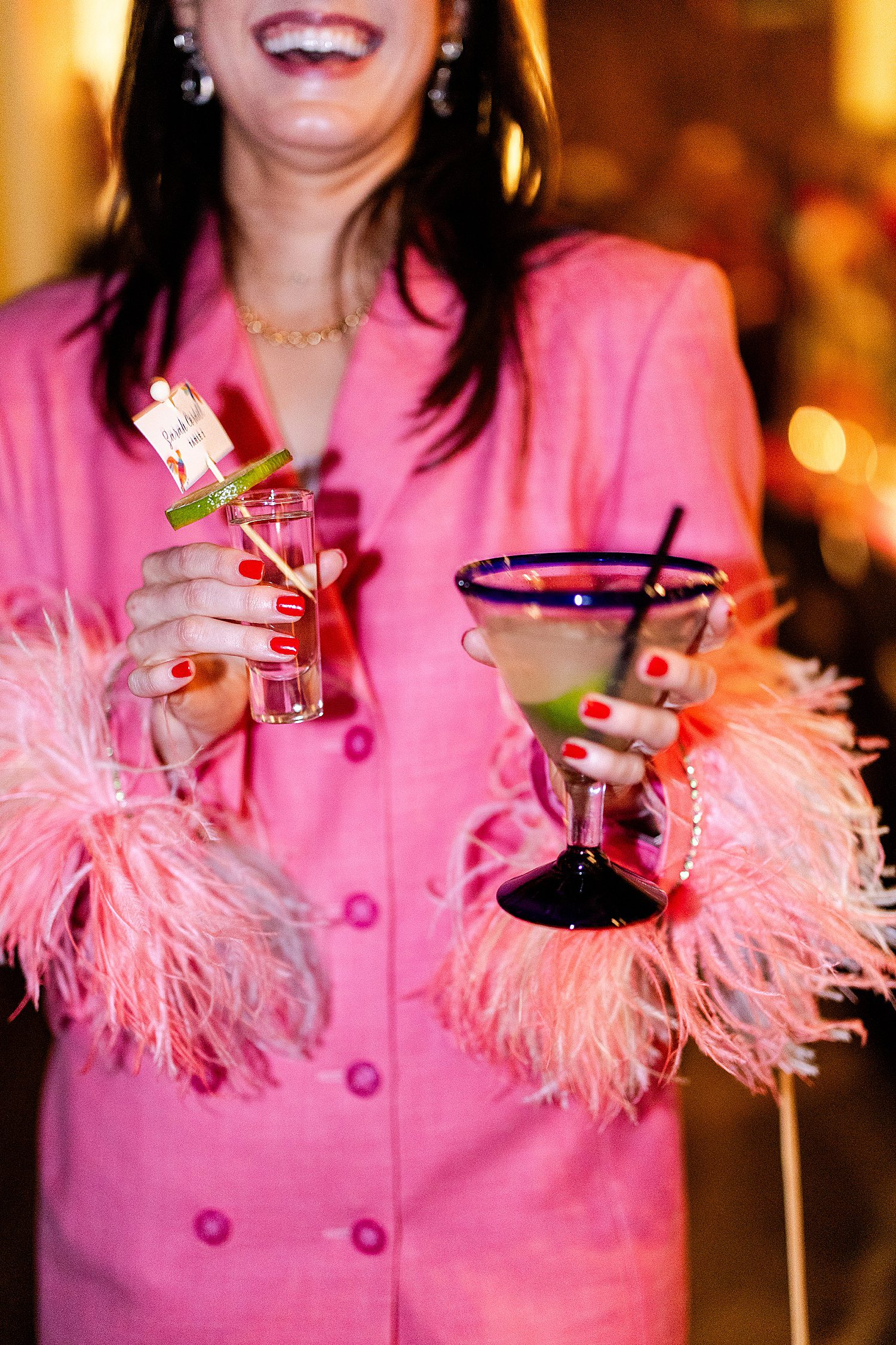 Woman in pink coat holding margarita and a tequila shot