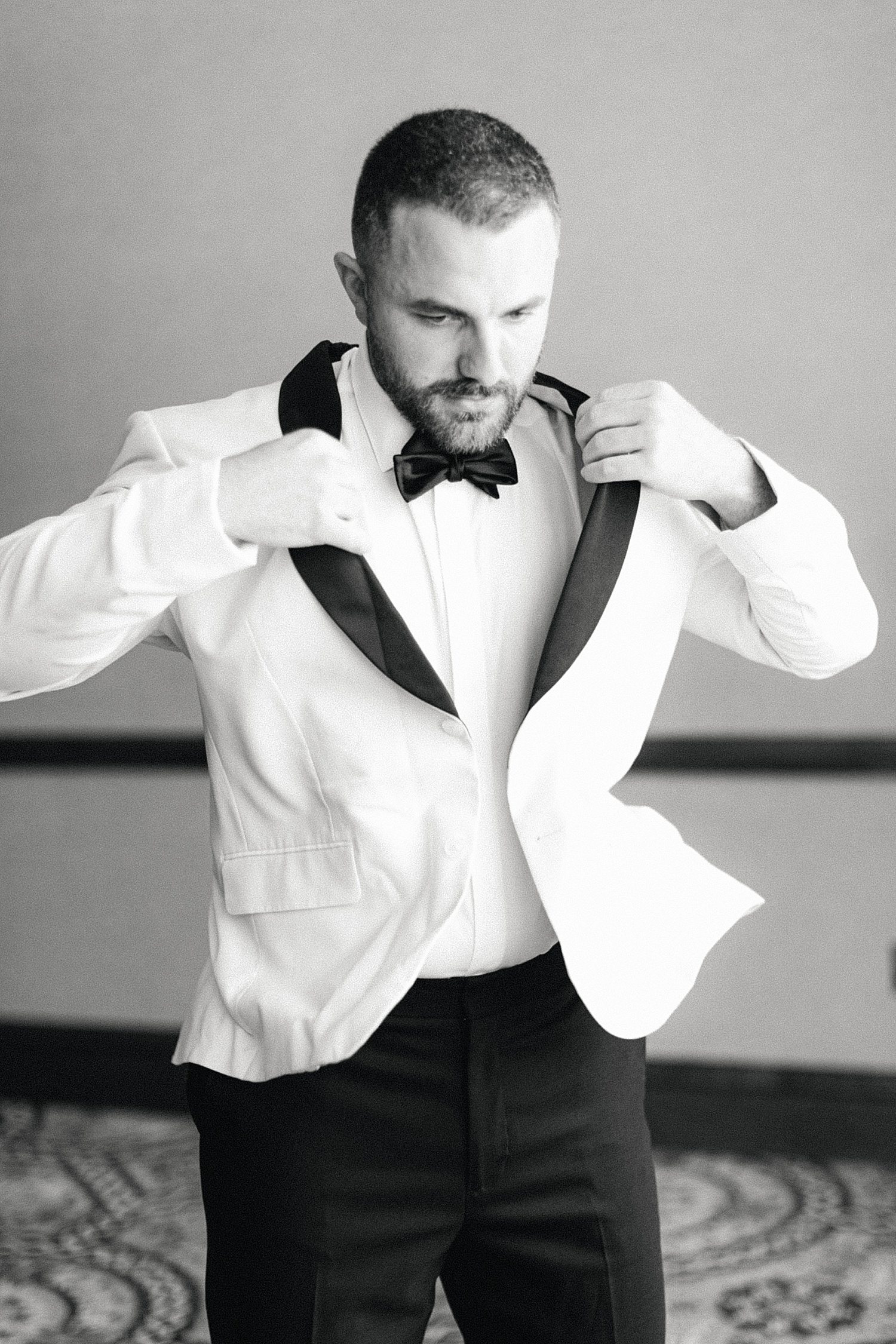 Groom putting on his white tuxedo jacket with black lapels